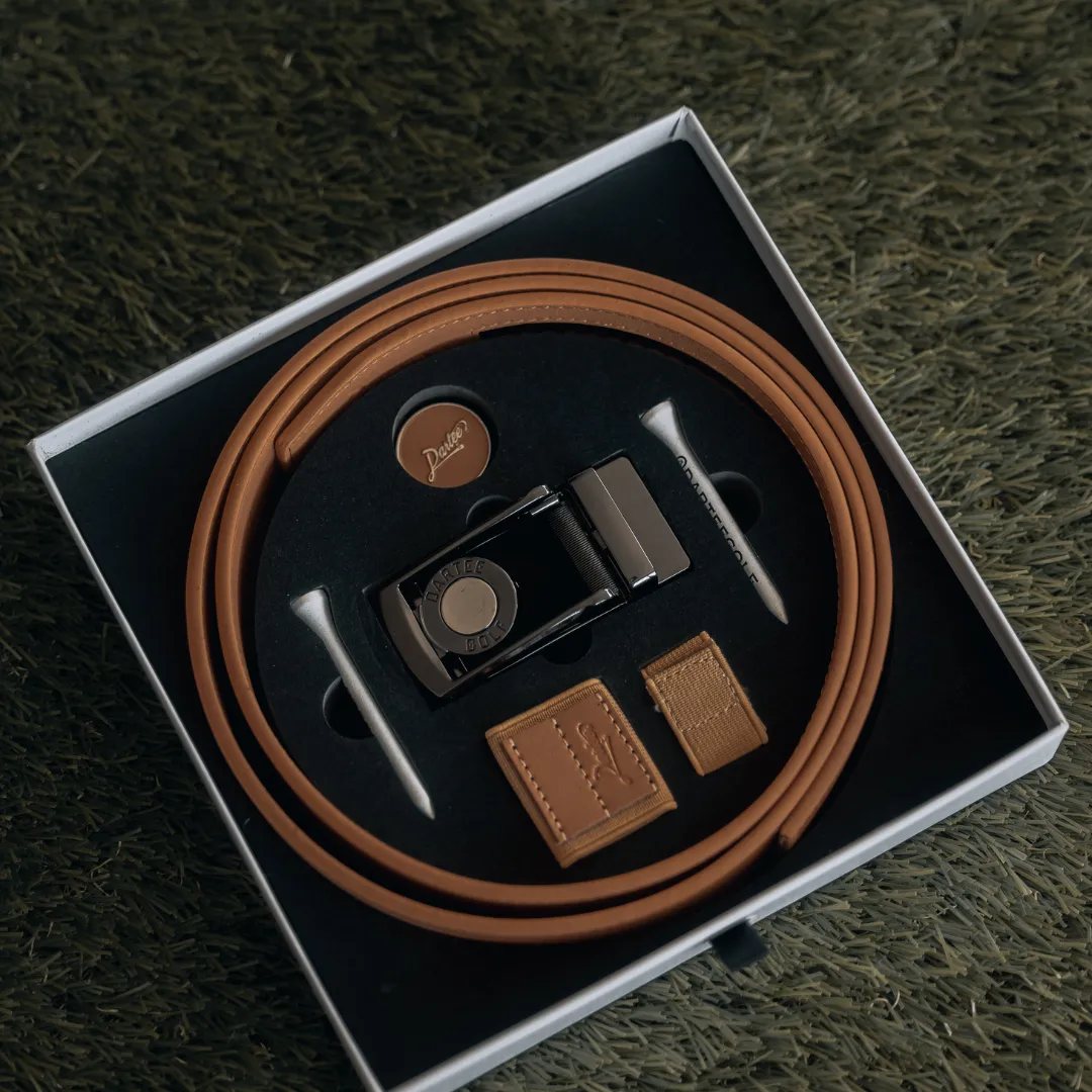 Brown belt set with buckle and accessories in a box on grass.