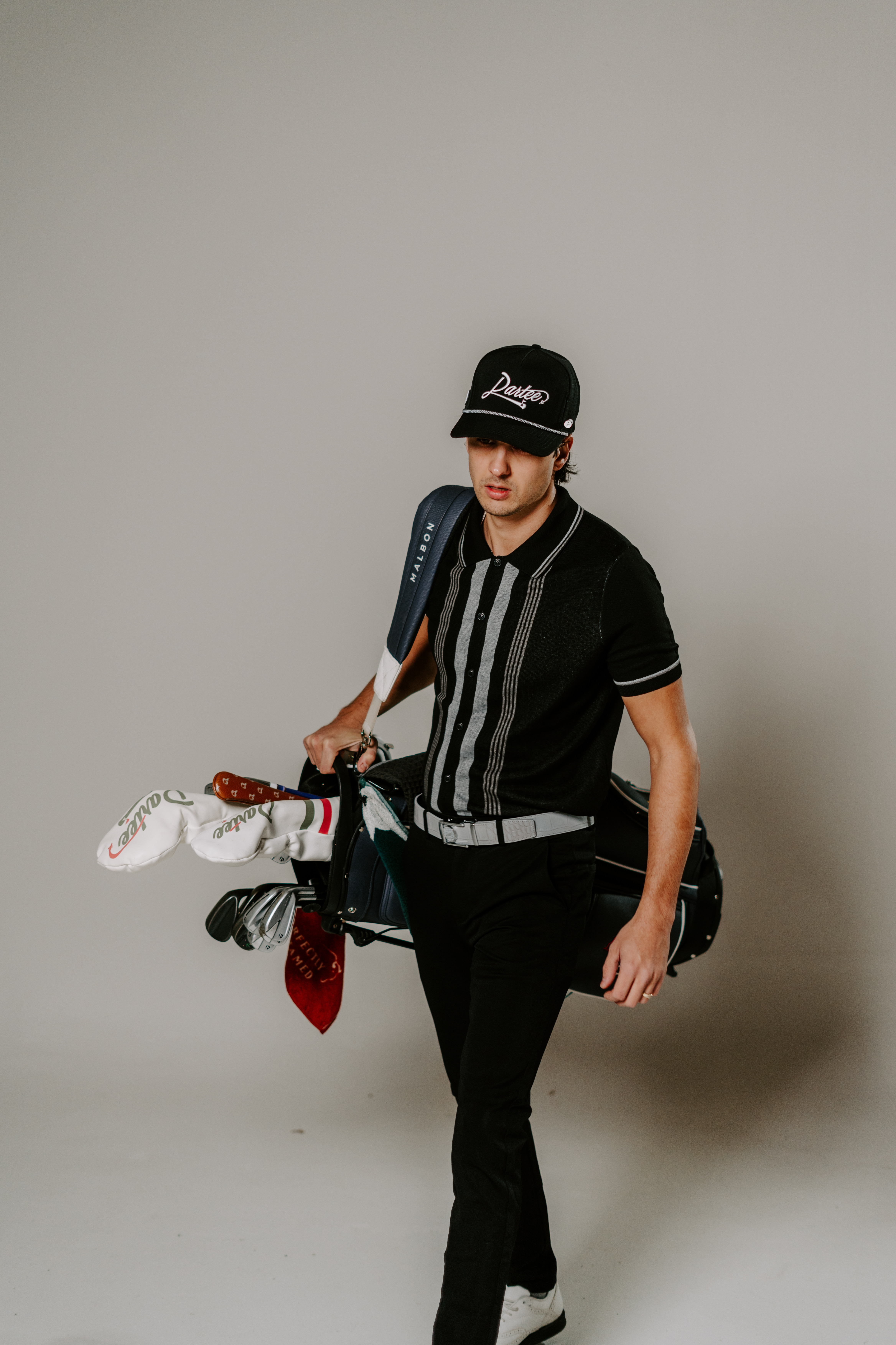 Person in black outfit carrying a golf bag against a plain background.