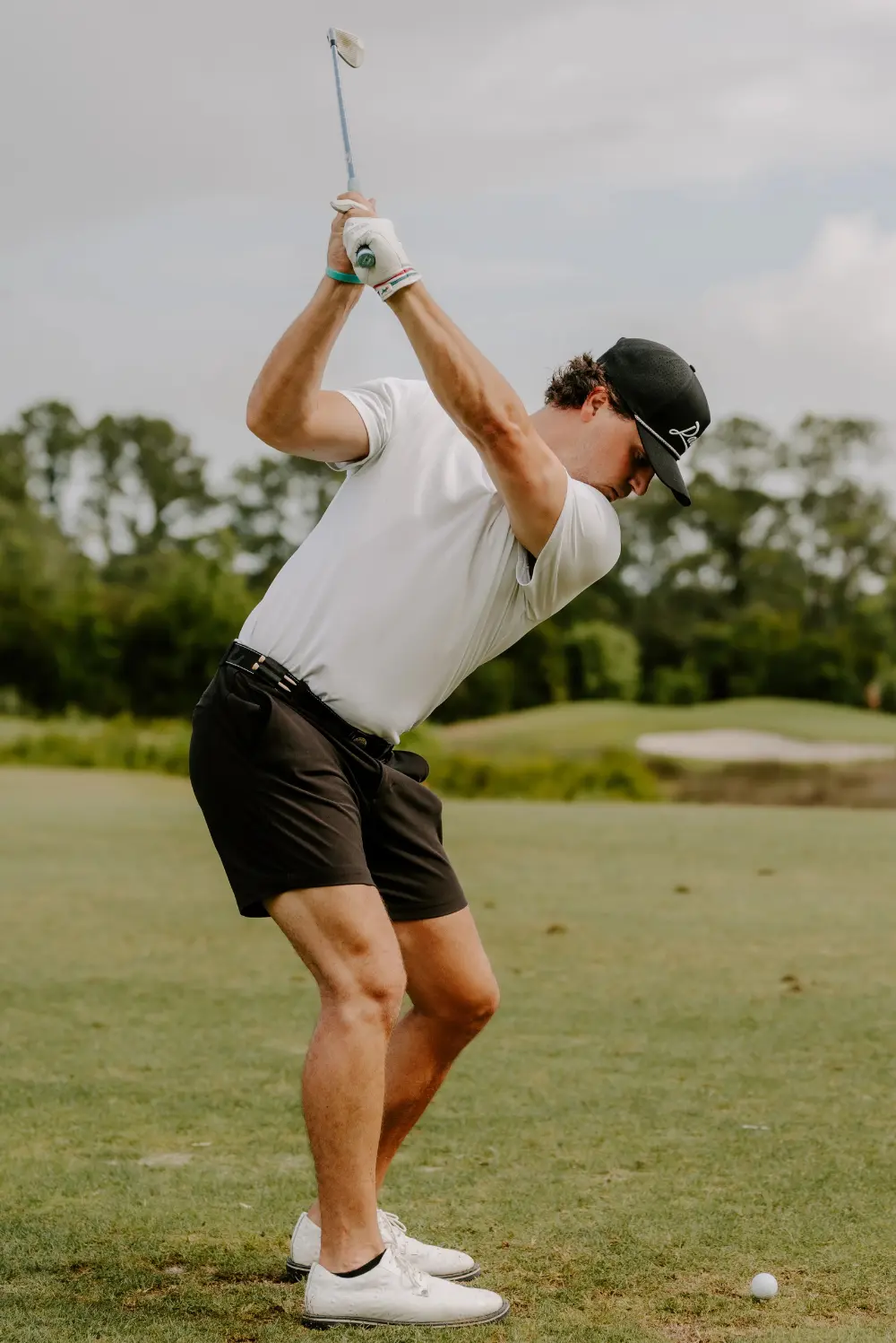 A person in mid-golf swing on a grassy course.