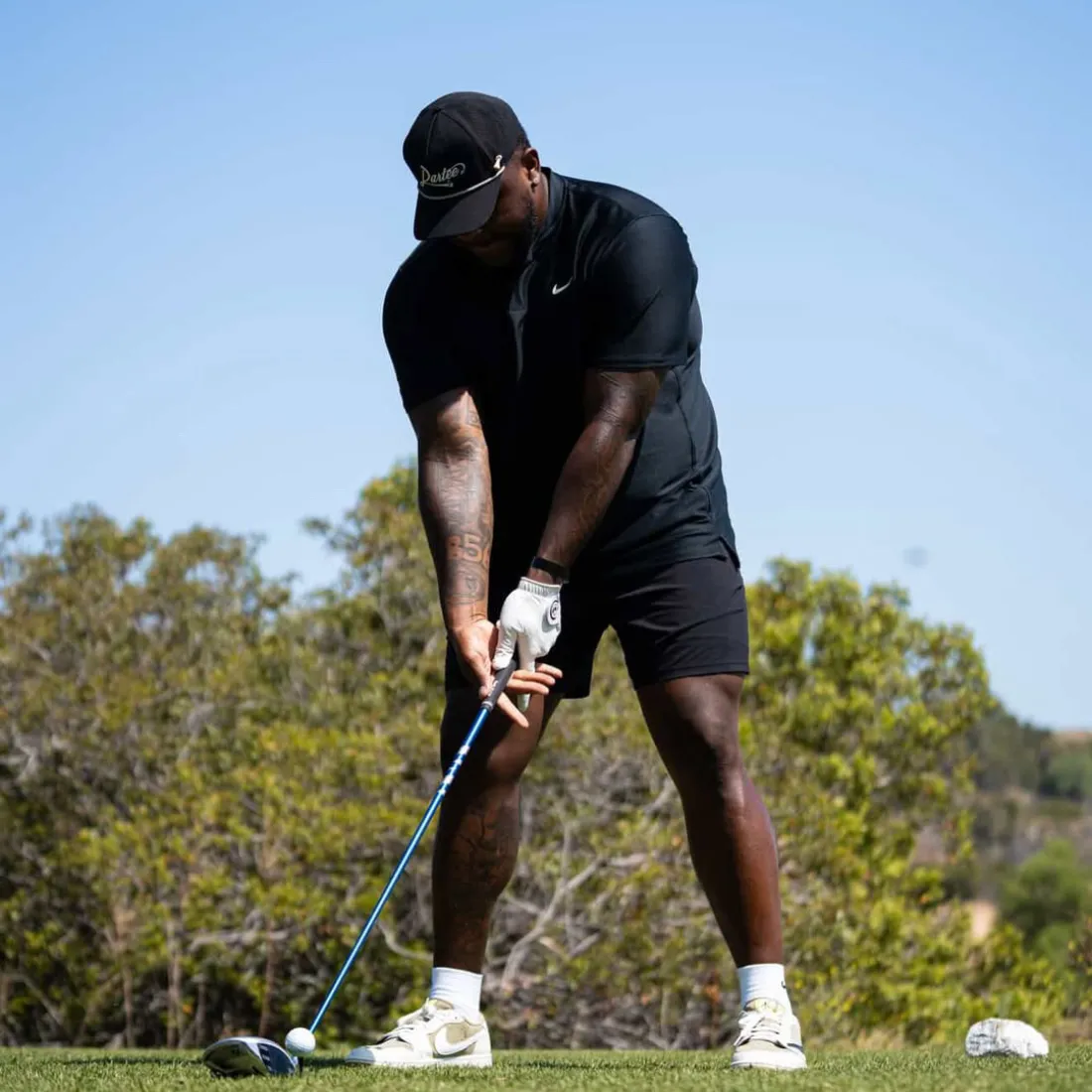Person in black outfit playing golf on a sunny day.