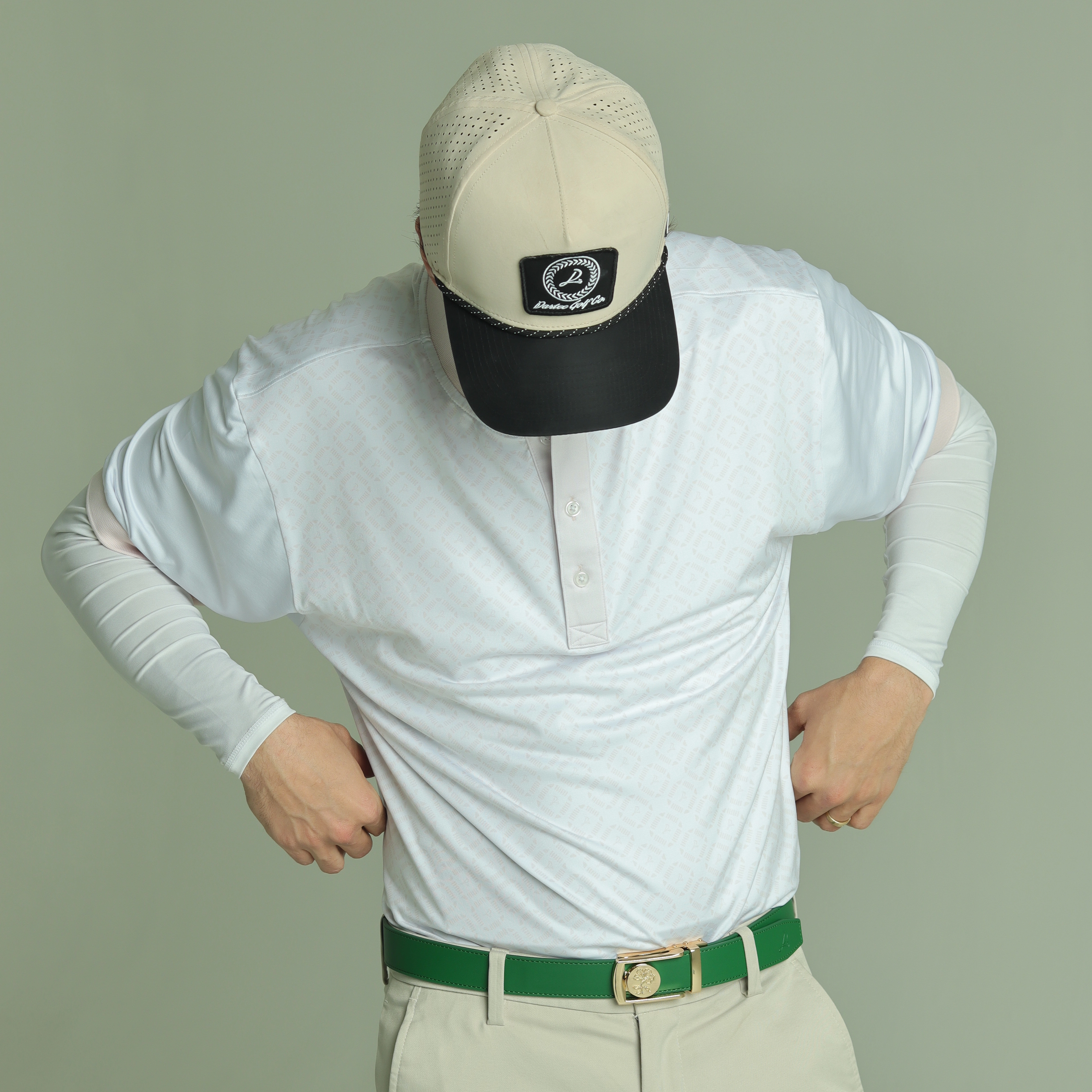 Person in white shirt and cap adjusting clothing, with a green belt.