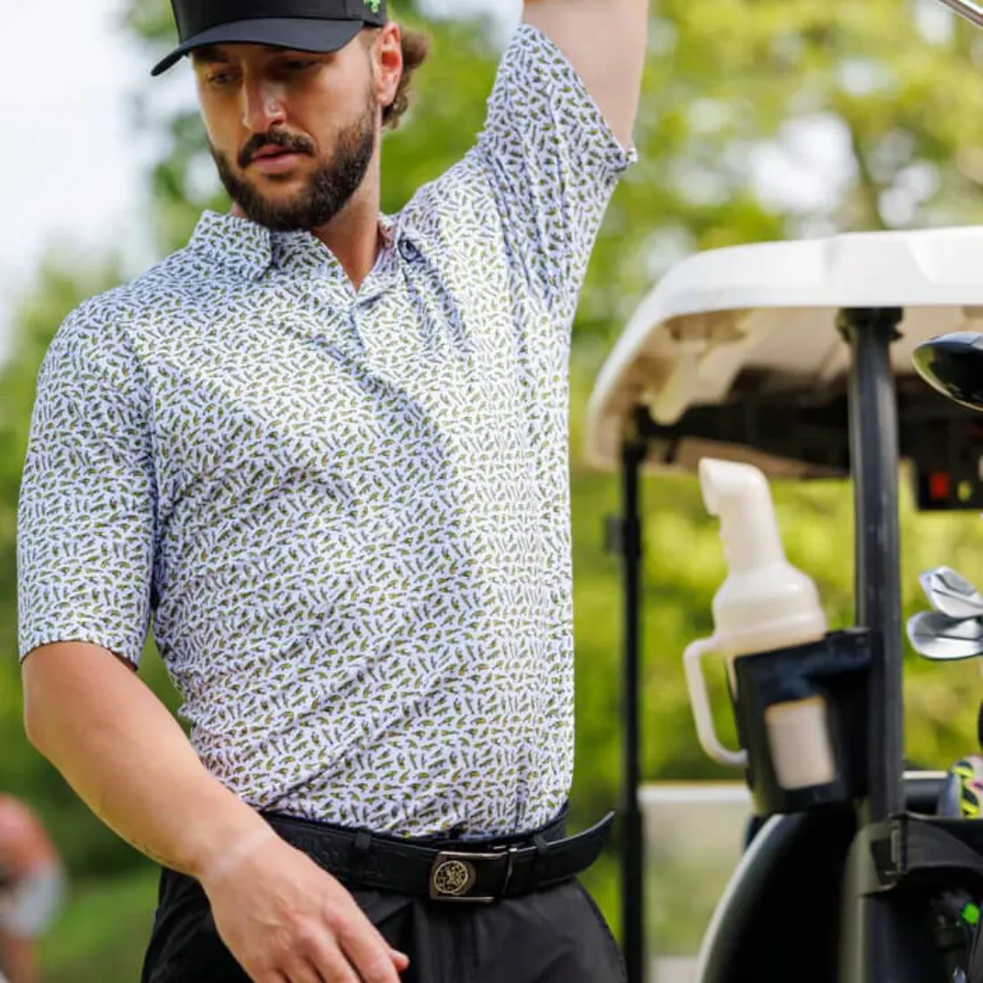 Man in patterned shirt and cap standing by a golf cart.
