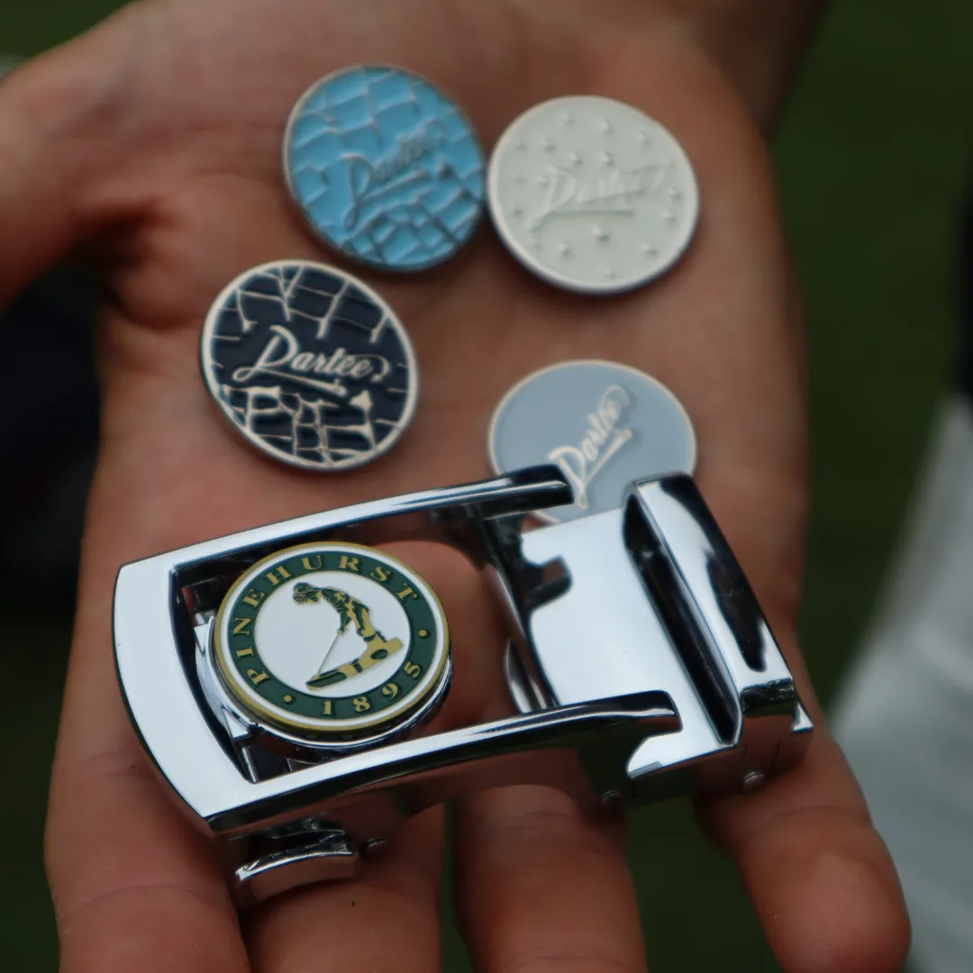 Hand holding golf ball markers and a Pinehurst clip.