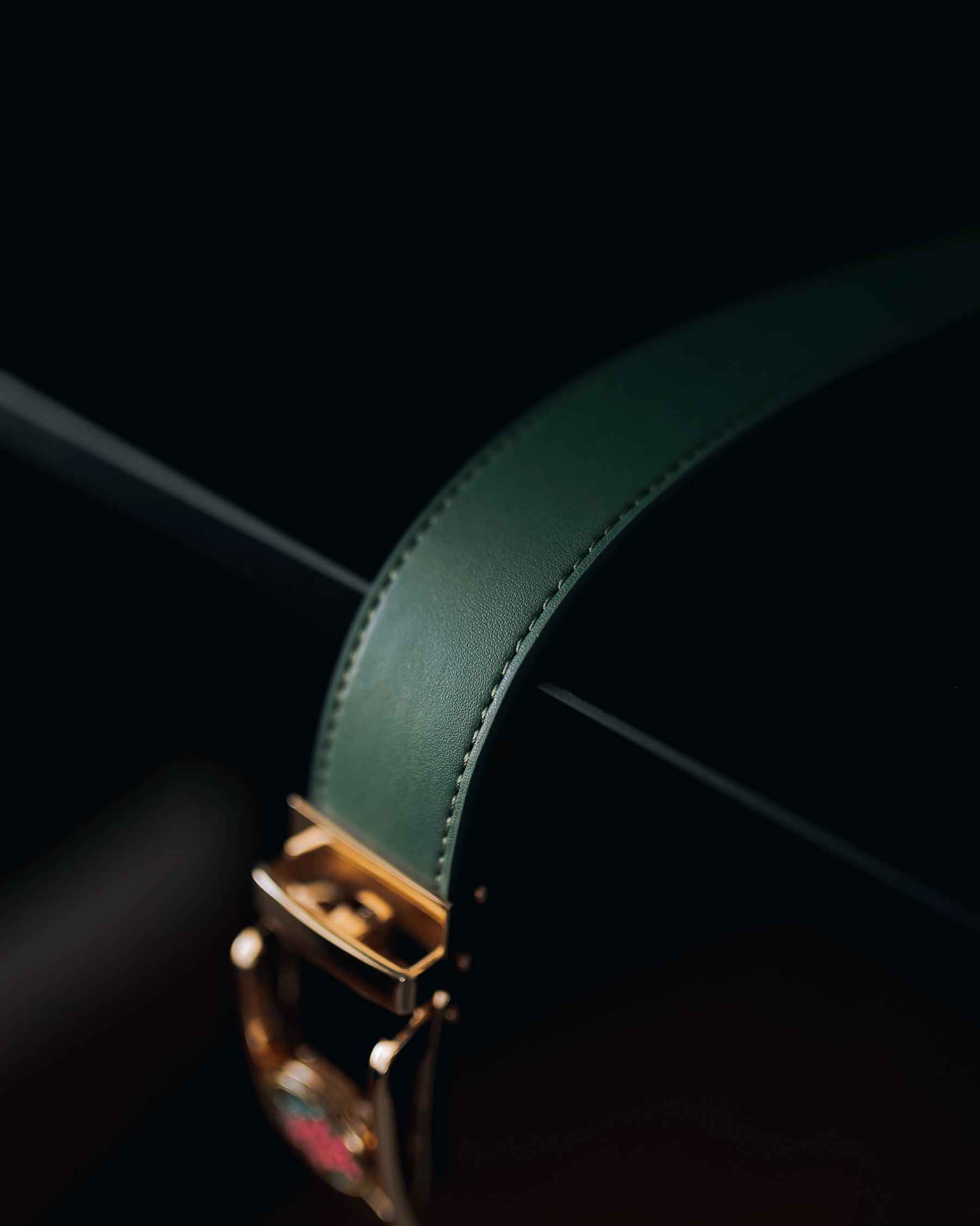 Close-up of a green leather watch strap with a gold buckle.