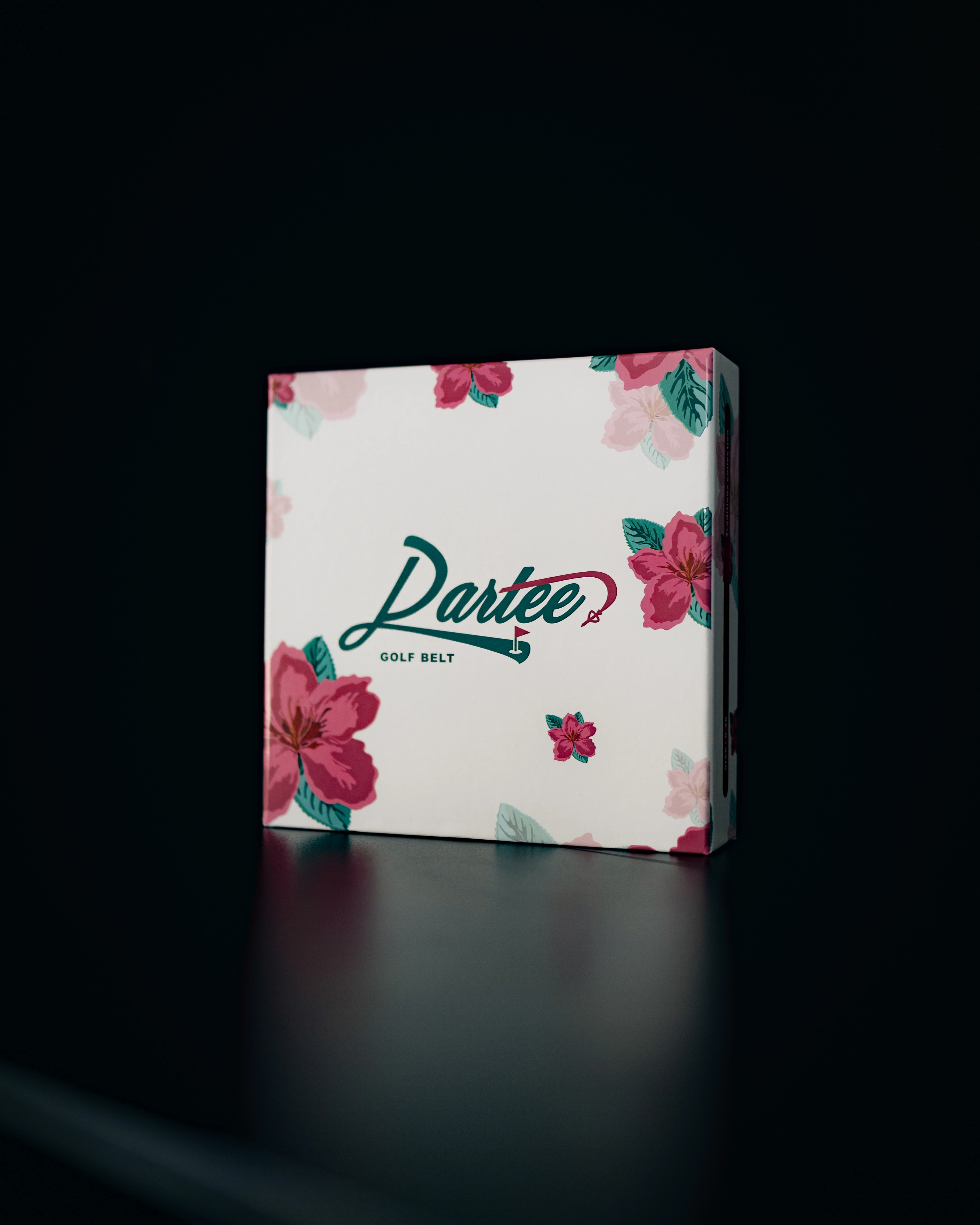 A white box with a pink floral pattern and the logo 'Dartee Golf Belt' on a black surface.