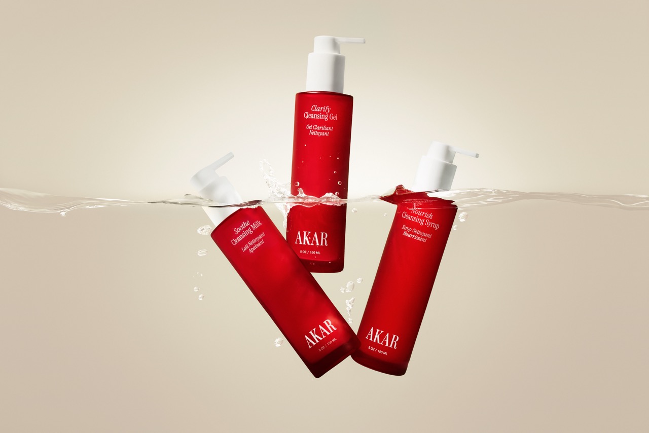 Three Akar skincare bottles, including cleansing gel, milk, and syrup, float partially submerged in water.