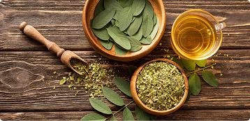 An overhead shot of fresh and dried tea leaves in wooden bowls next to a cup of tea.