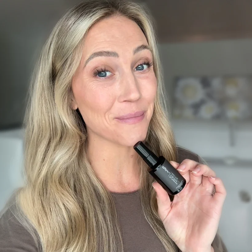 Person holding a small black bottle, smiling at the camera.