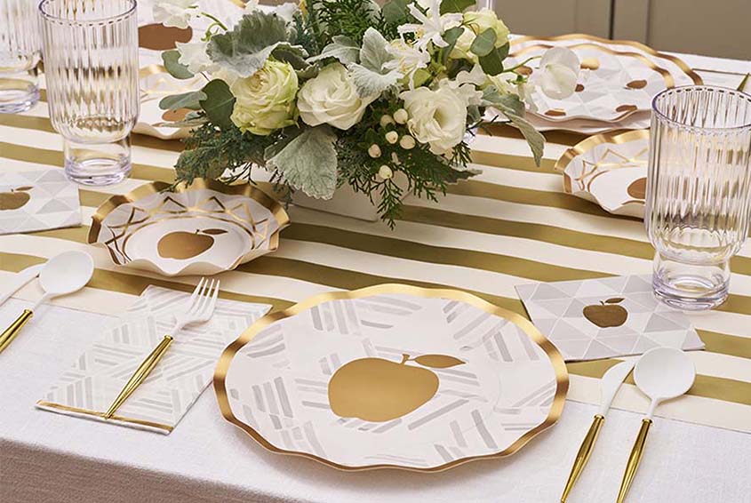 Elegant table setting with gold apple-themed plates and white flowers centerpiece.