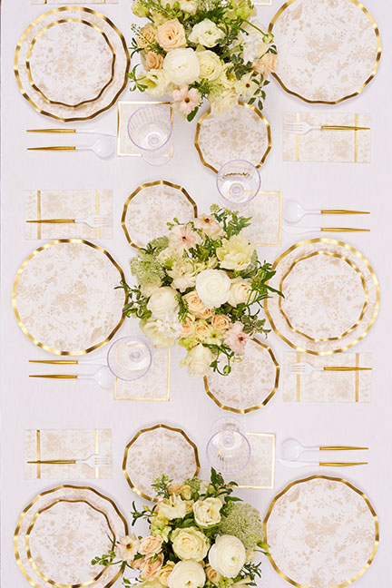 An overhead view of a table set with floral paper plates, gold cutlery, and bouquets of flowers.