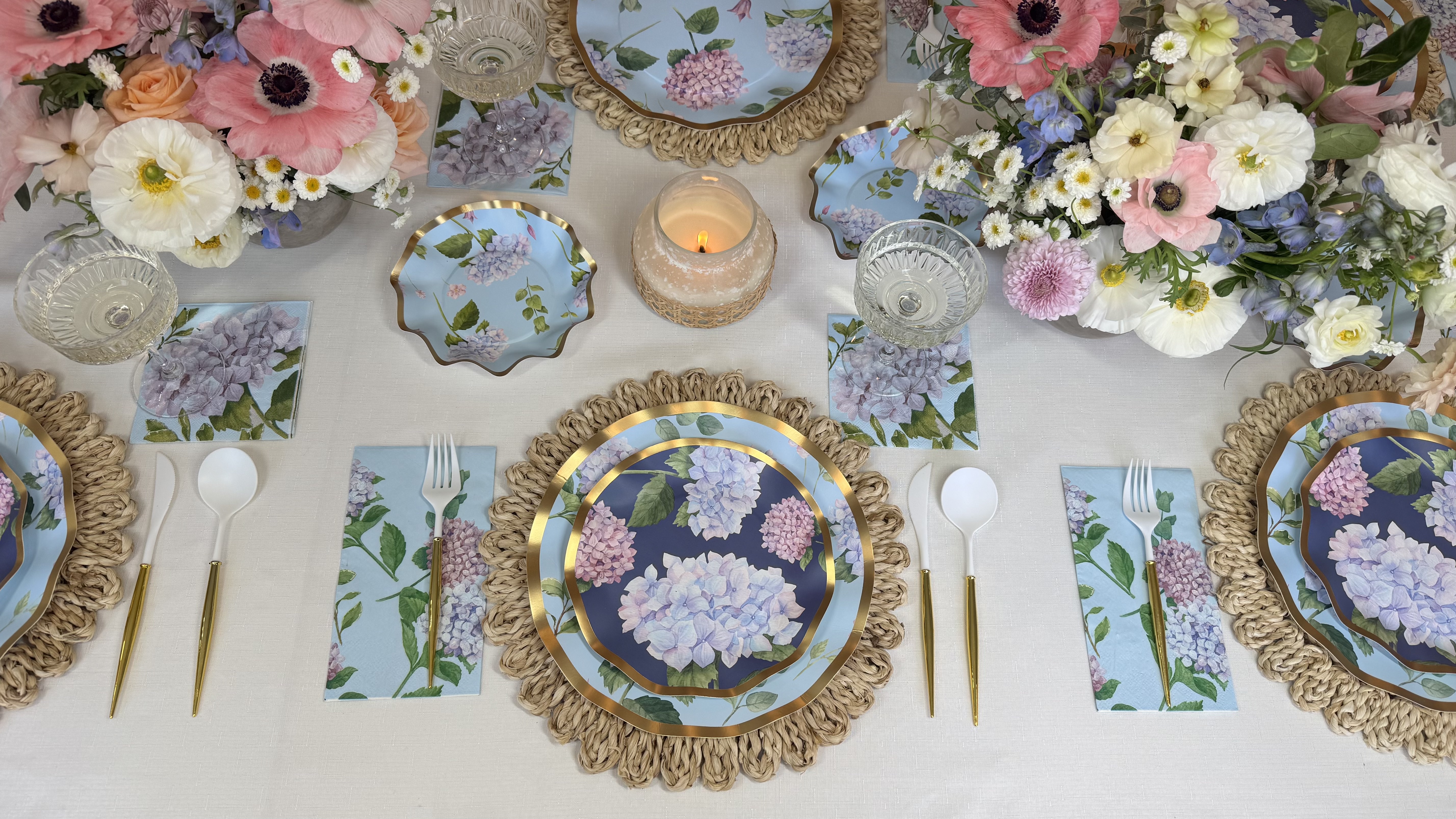Elegant table setting with floral plates, candles, and colorful flower arrangements.