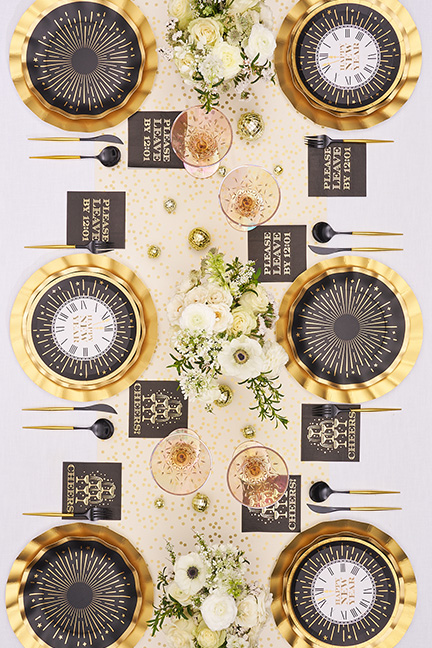 An overhead view of a festive New Year's Eve table setting with black and gold party supplies.