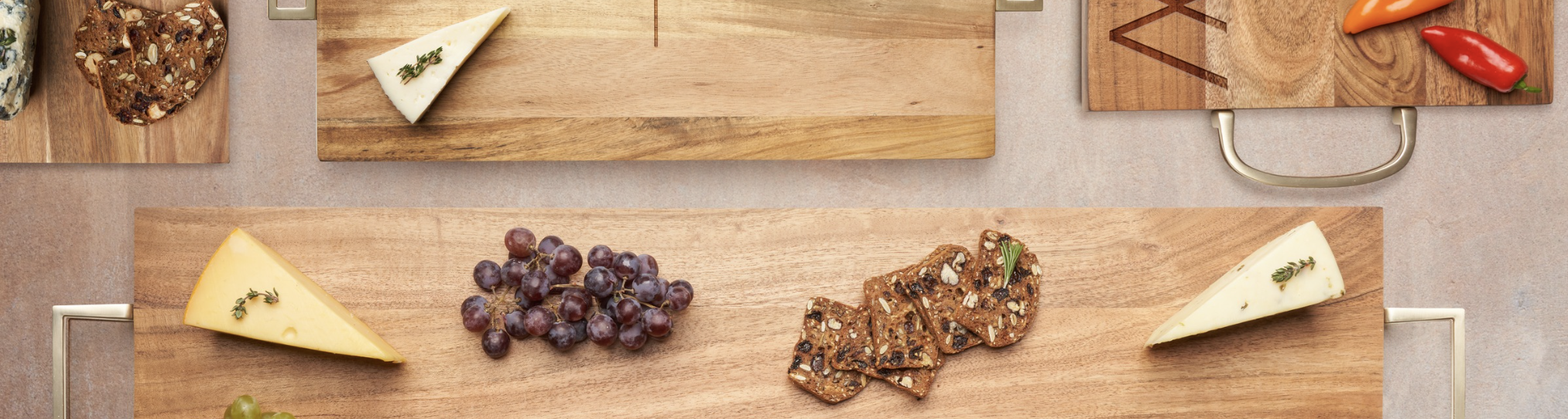 Wooden boards with cheese, sliced bread, grapes, and peppers arranged artistically.