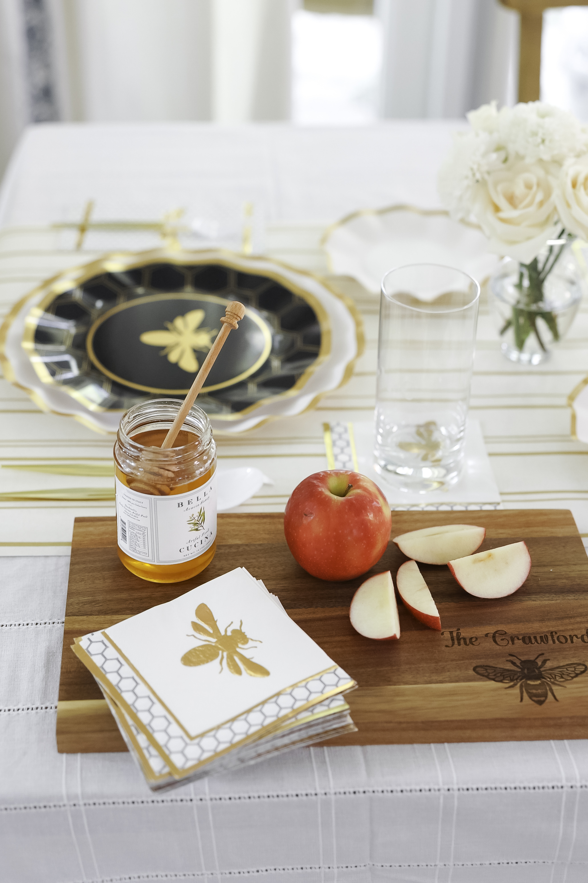 A bee-themed table setting with a jar of honey and sliced apples on a wooden board.