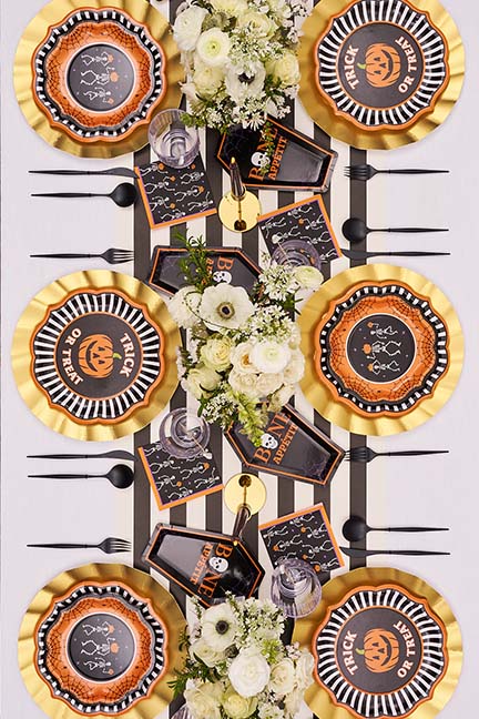 An overhead view of a Halloween tablescape with themed plates, black cutlery, and a white floral centerpiece.