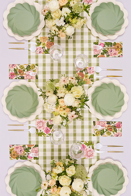 An overhead view of a table set with green gingham, floral napkins, and scalloped green plates.