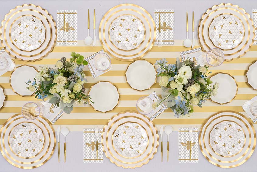 Elegant table setting with gold-striped plates, floral arrangements, and gold cutlery.