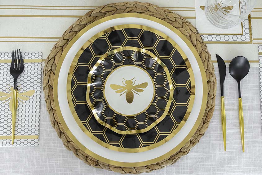 Bee-themed table setting with black and gold plates, cutlery, and napkin.