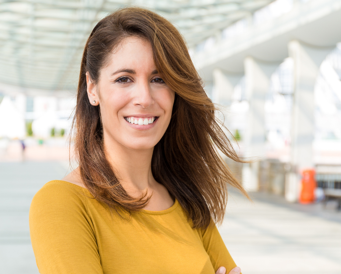 Woman in yellow shirt smiling in a bright, modern architectural setting.
