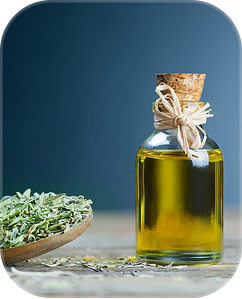 A small glass bottle of oil with a cork stopper sits next to a wooden spoon of dried herbs.