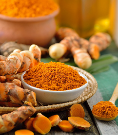 A bowl of ground turmeric powder surrounded by fresh turmeric root, both whole and sliced.