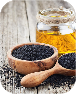 A wooden bowl and spoon filled with black seeds sit next to a small glass jar of oil.