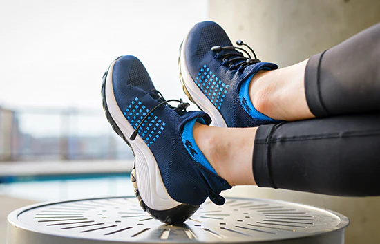 Person wearing blue athletic shoes resting feet on a metal surface.