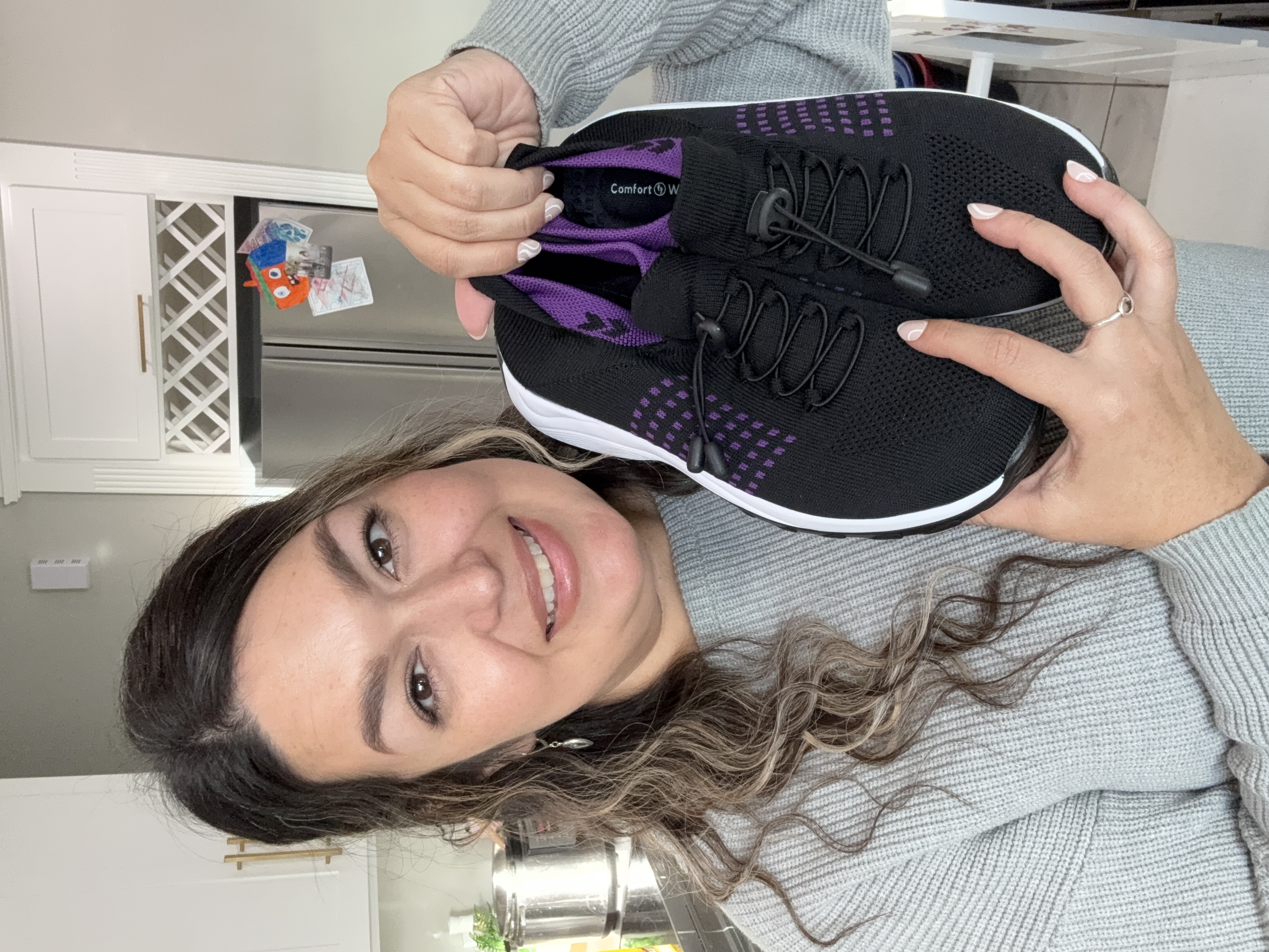 Person holding a pair of black and purple sneakers in a kitchen.