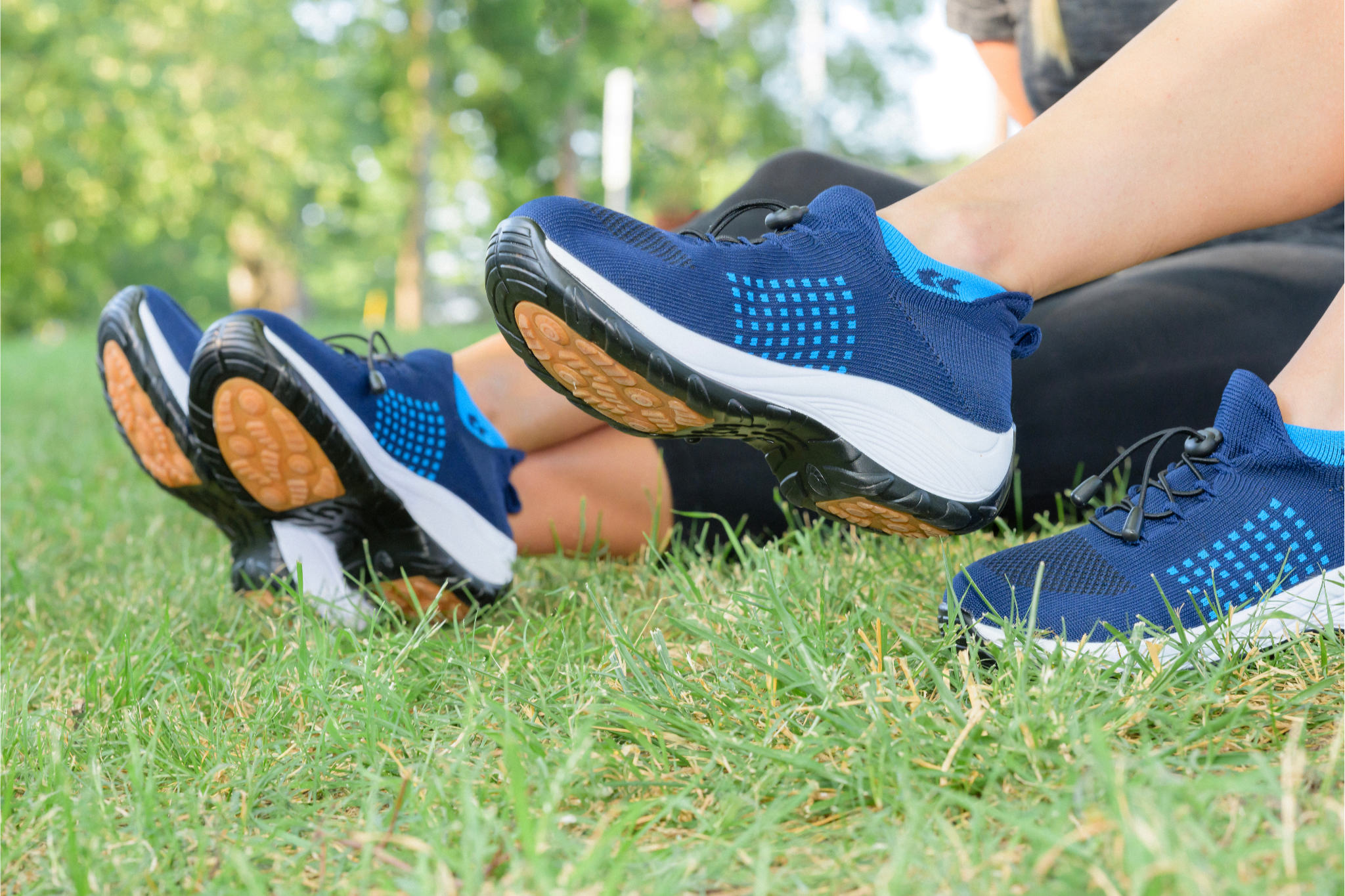 Two people wearing blue athletic shoes sitting on grass.