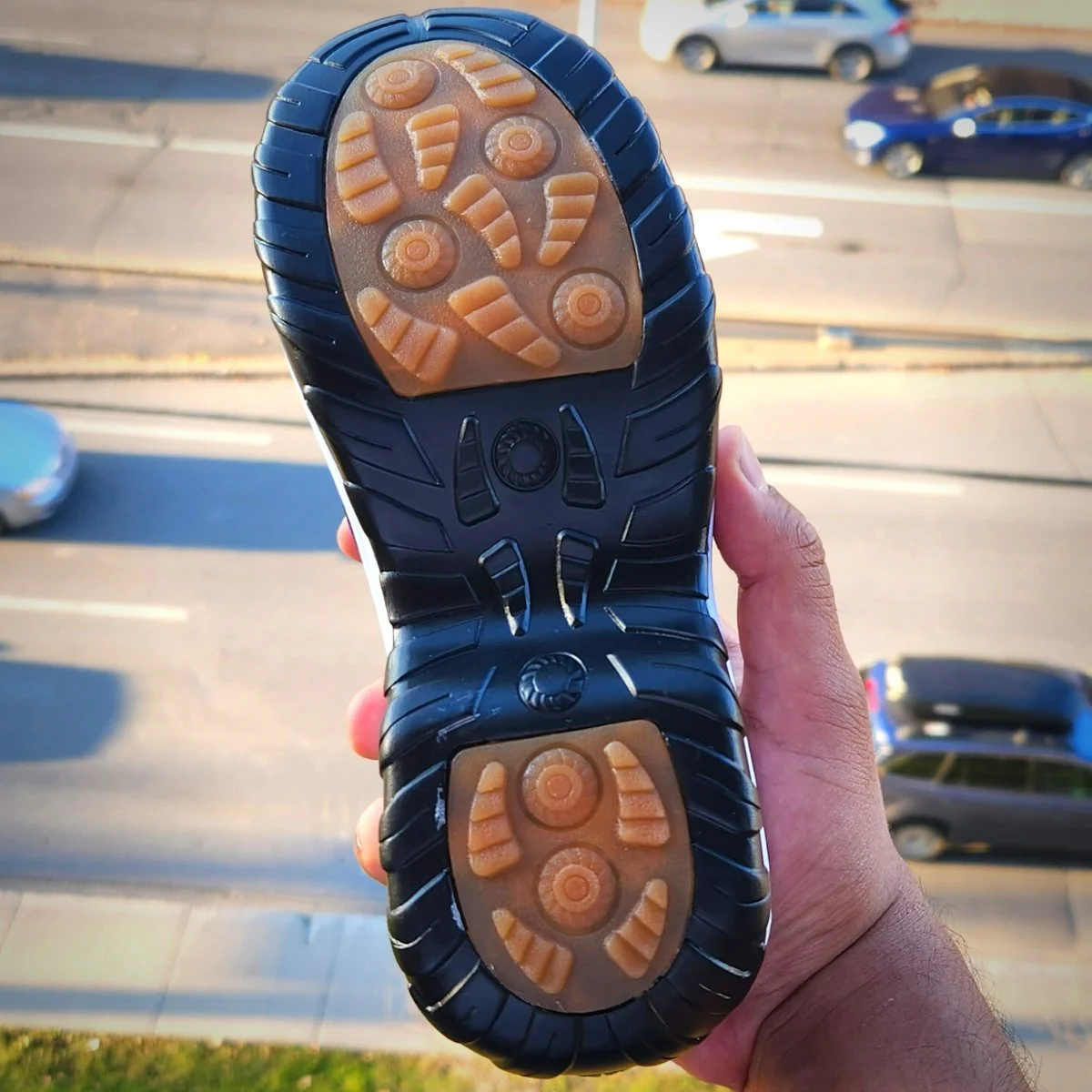 Close-up of a shoe sole with a road and cars in the background.