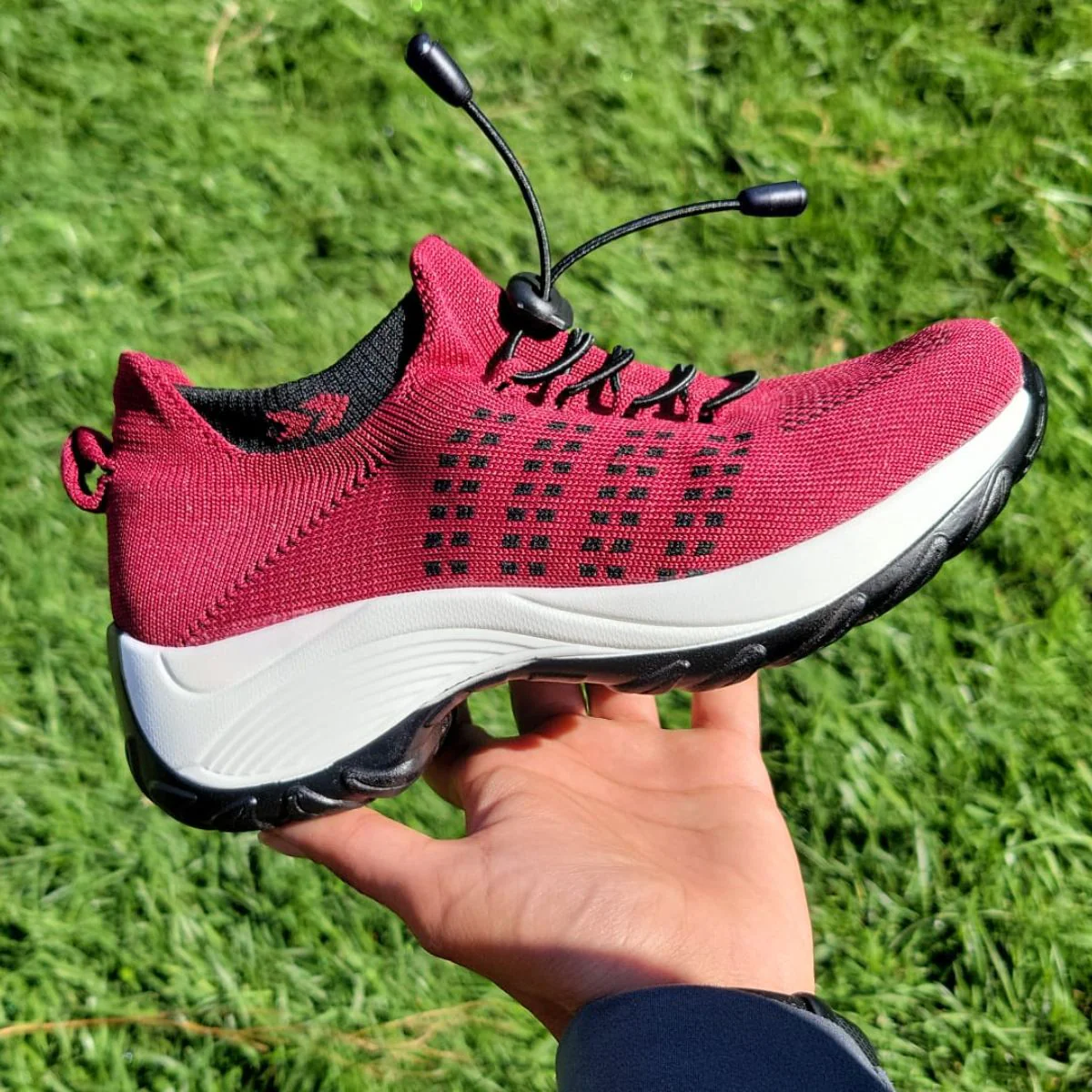 A hand holding a red athletic shoe with black laces and white sole.
