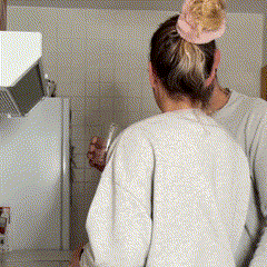 Two people in a kitchen, one playfully balancing a glass on the other's head.
