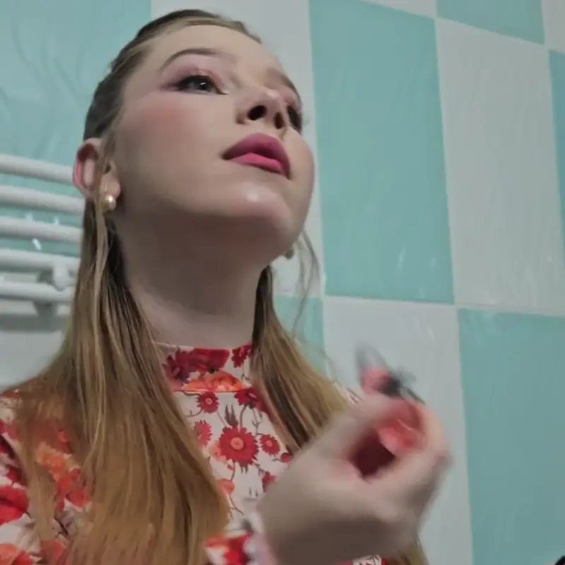 Person looking upward, applying makeup in a bathroom with a floral top.