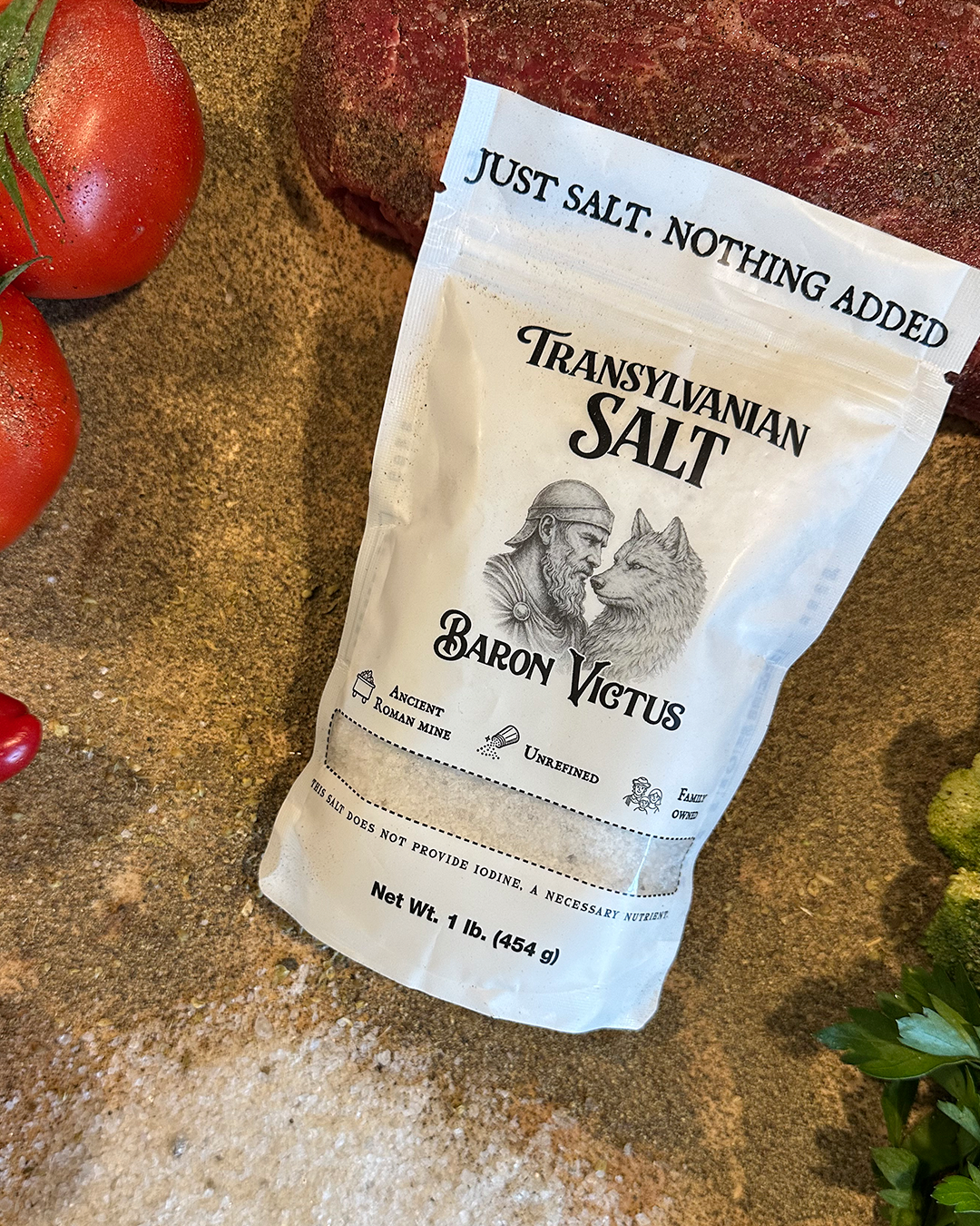 A white bag of Baron Victus Transylvanian Salt sits on a stone surface next to fresh ingredients.