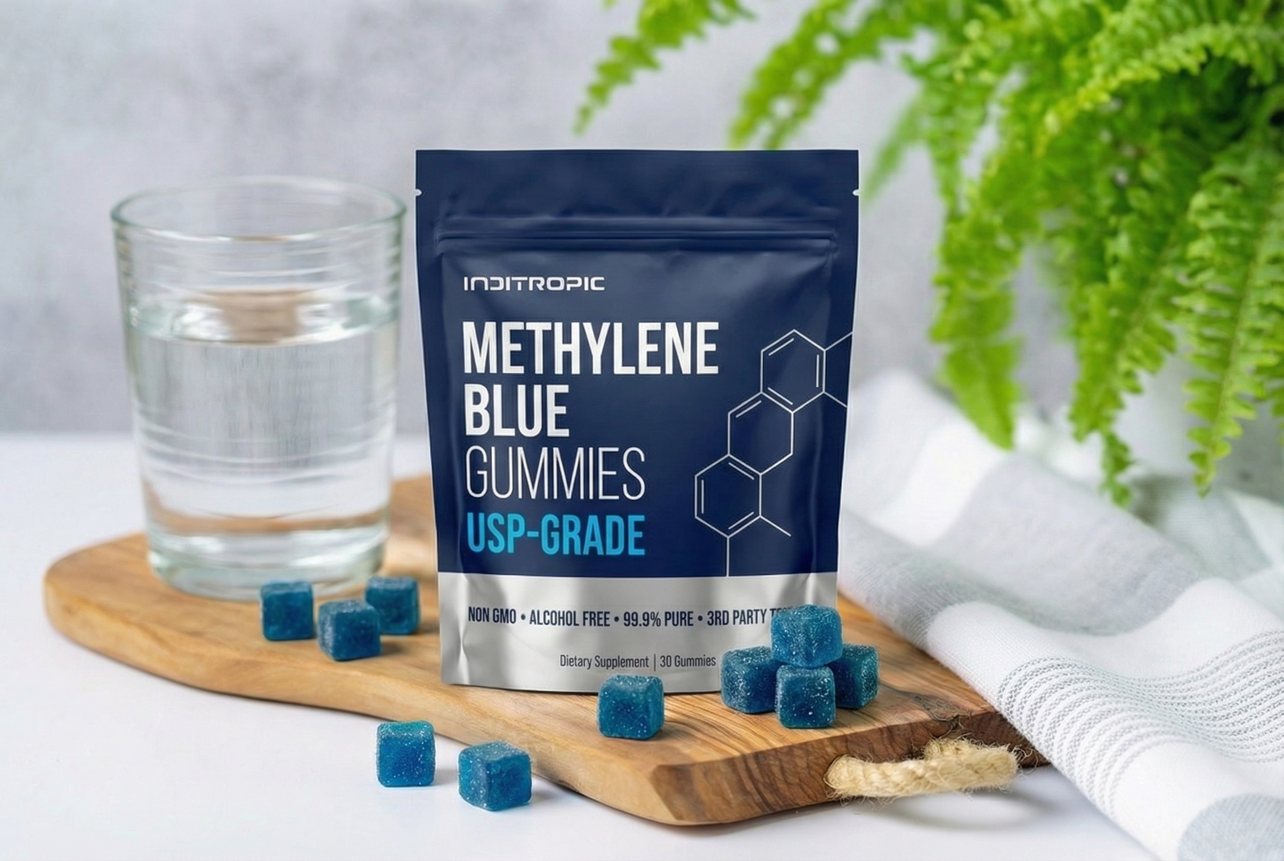 A pouch of Inditropic Methylene Blue Gummies on a wooden board next to a glass of water.
