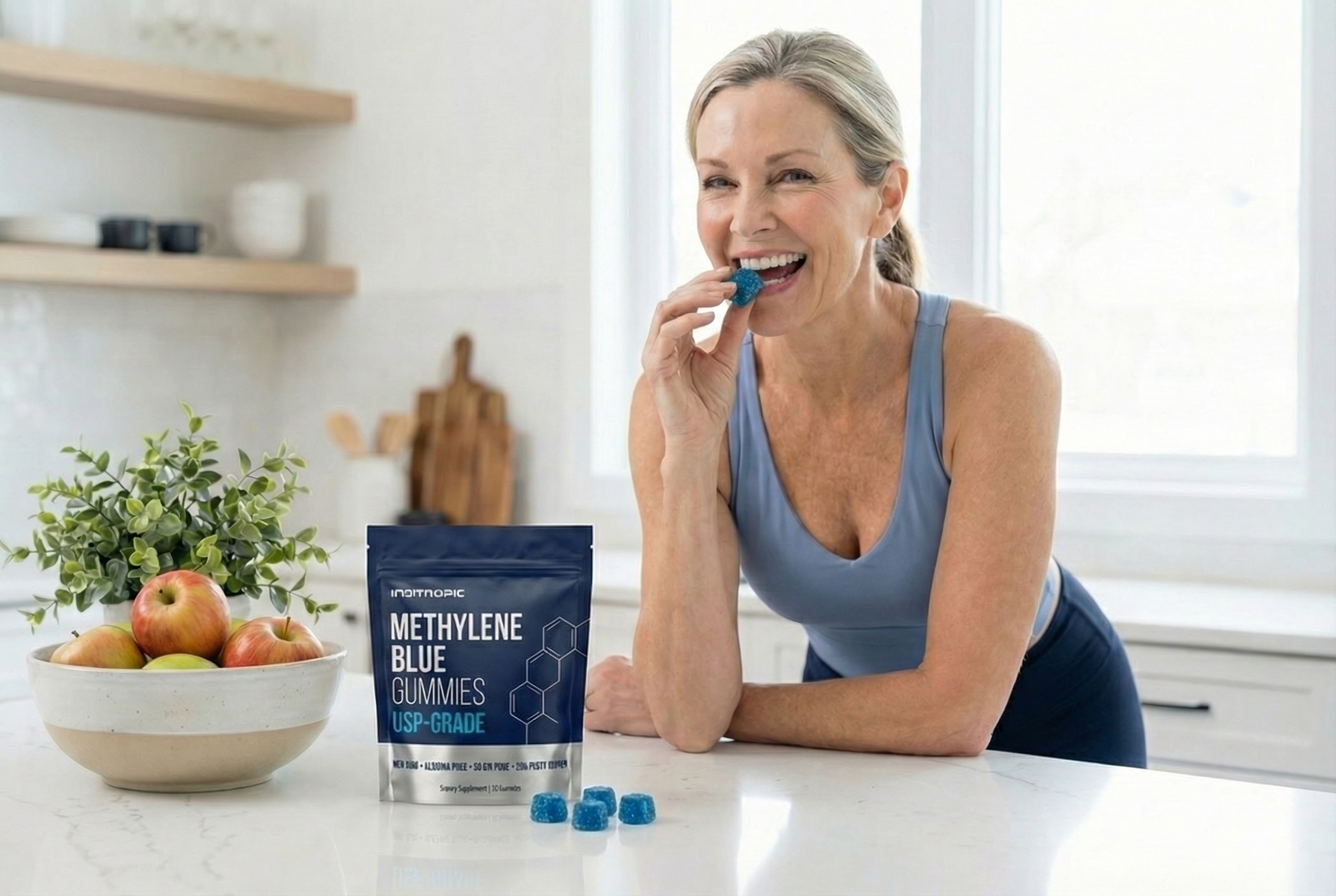 A smiling woman in a kitchen eats a blue gummy next to a pouch of Methylene Blue Gummies.
