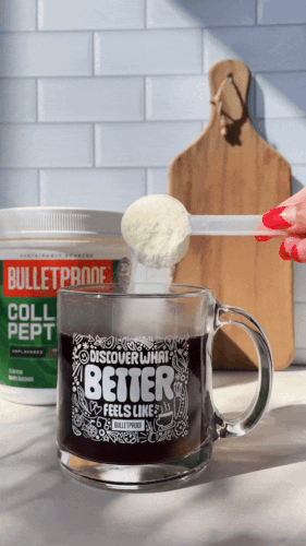 Scoop of powder being added to a mug of coffee on a kitchen counter.