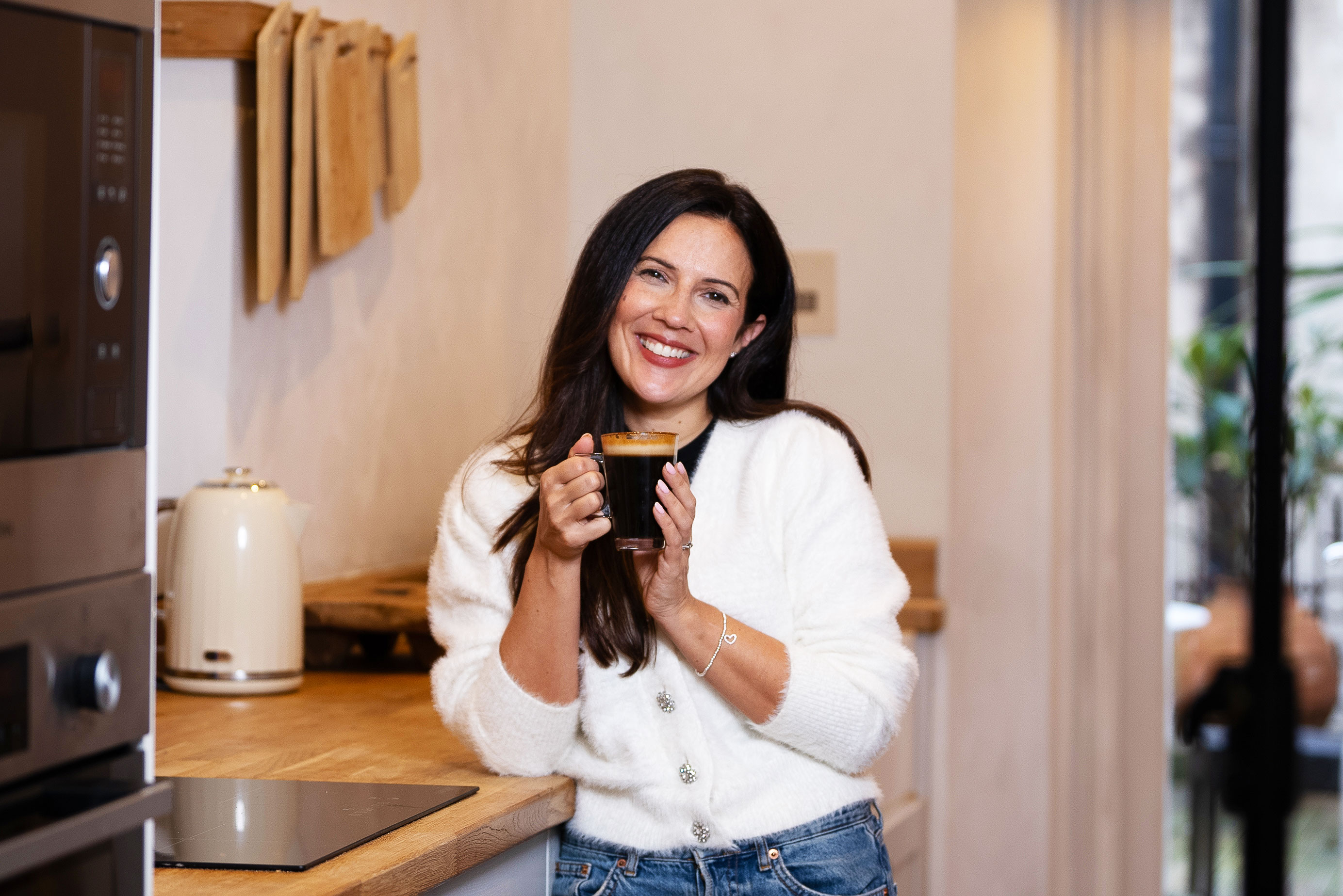Woman smiling while holding a cup of coffee in a kitchen.