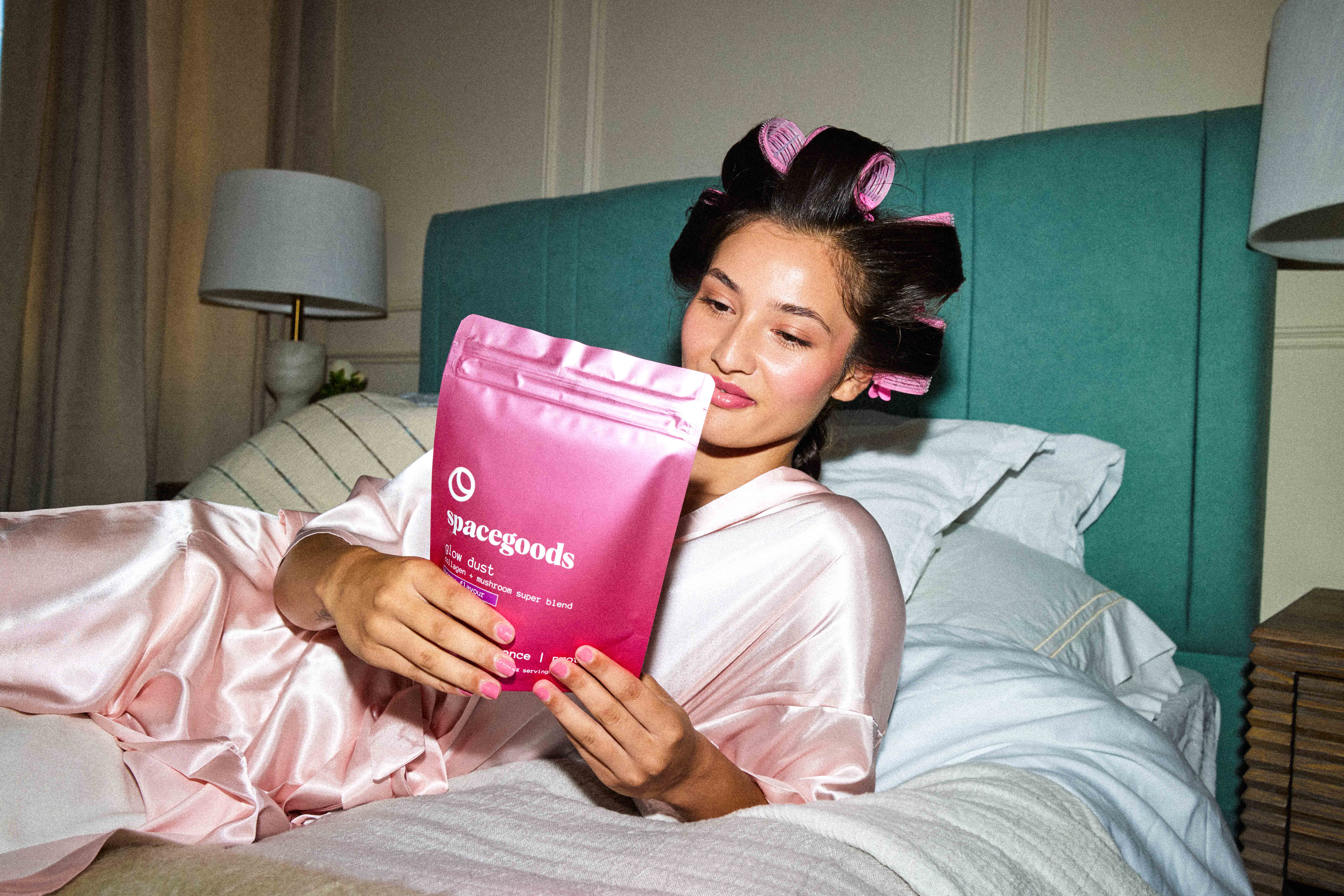 Person in bed with hair rollers, holding a pink Spacegoods bag.