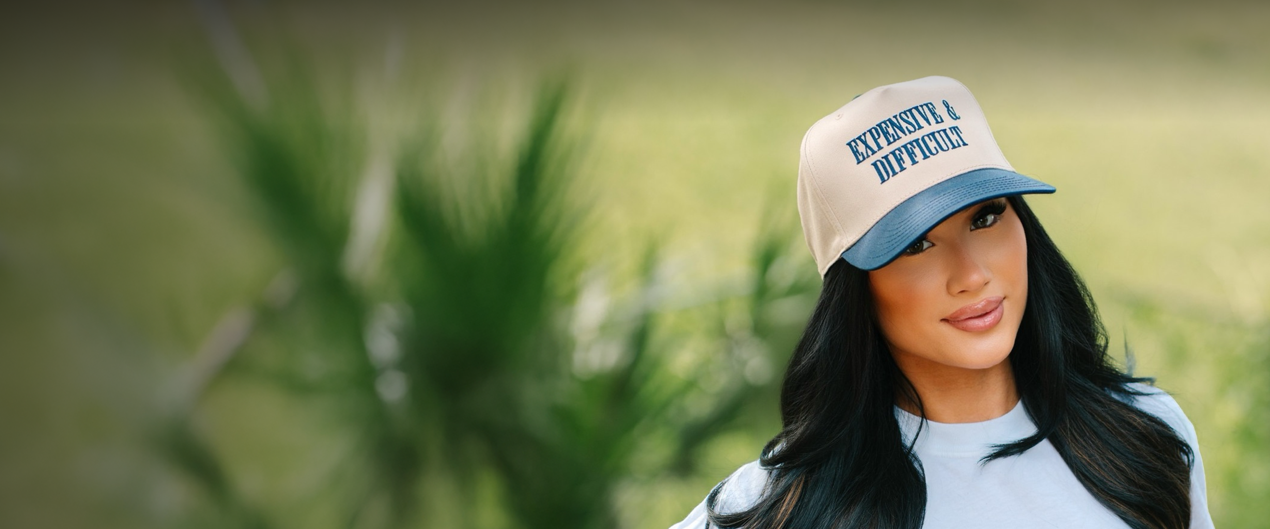 Person wearing a cap with 'Expensive & Difficult' text, smiling outdoors.