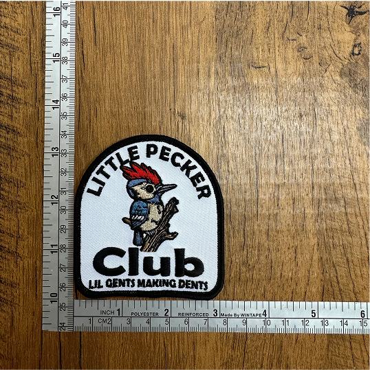 Patch with a woodpecker and text 'Little Pecker Club' on a wooden surface with rulers.