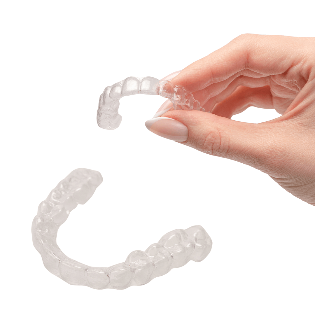 Hand holding a clear dental aligner with another aligner below.