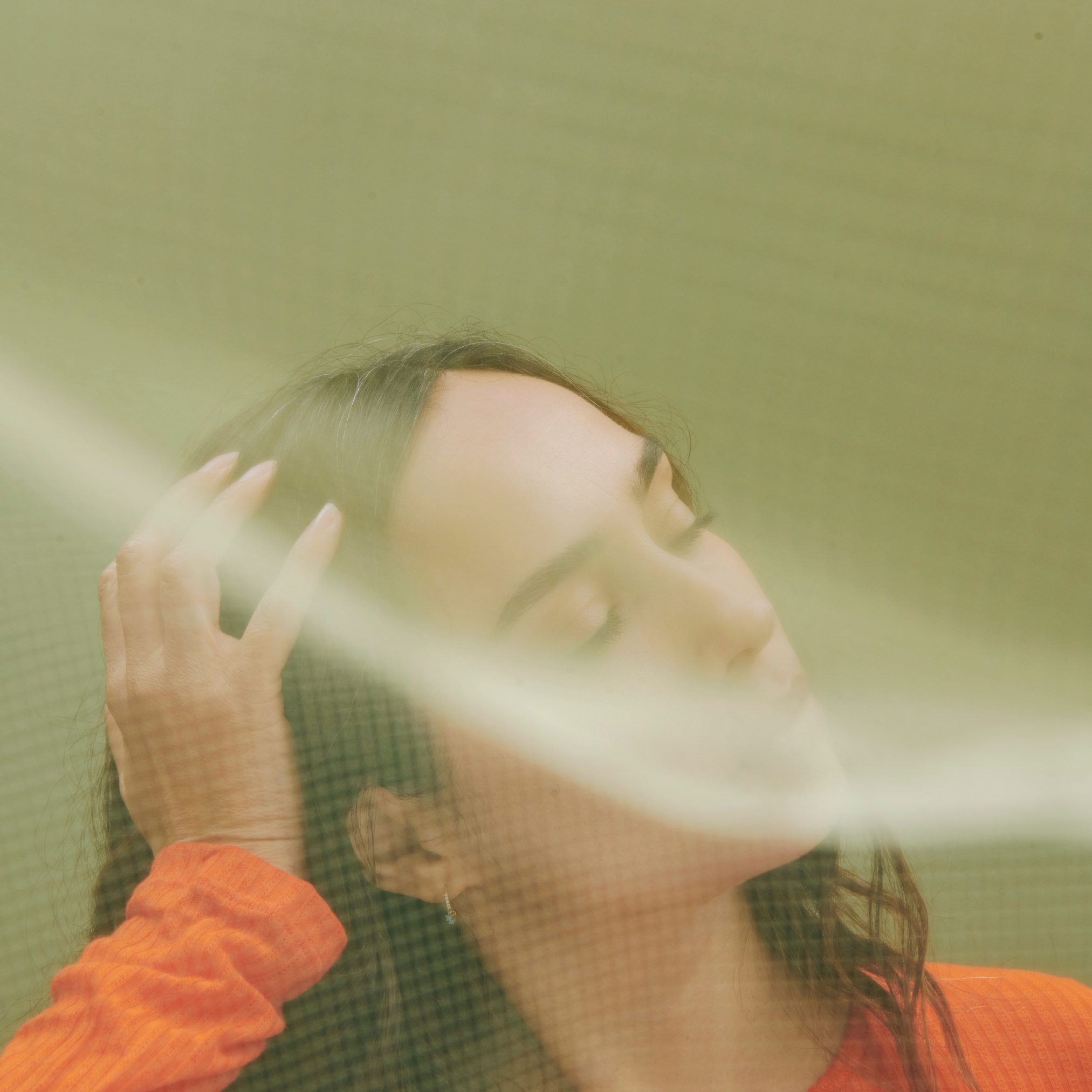 Person in orange shirt with closed eyes behind translucent surface.