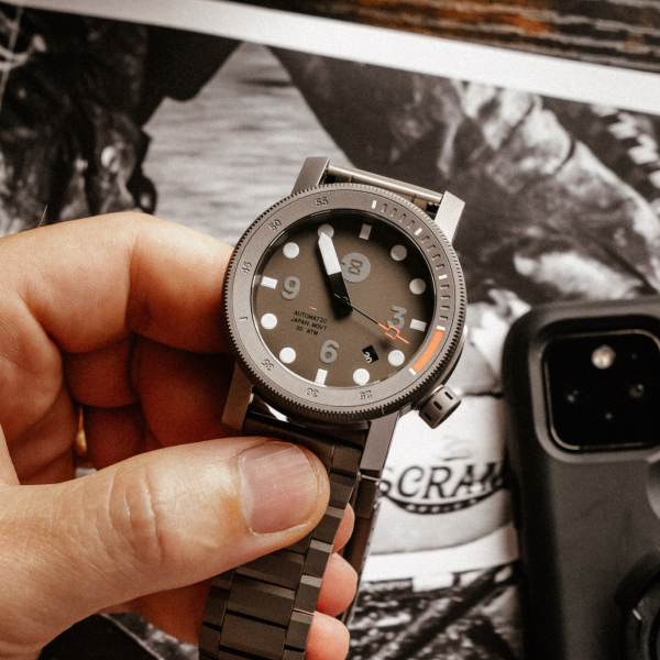 Close-up of a hand holding a metal wristwatch with an analog dial.