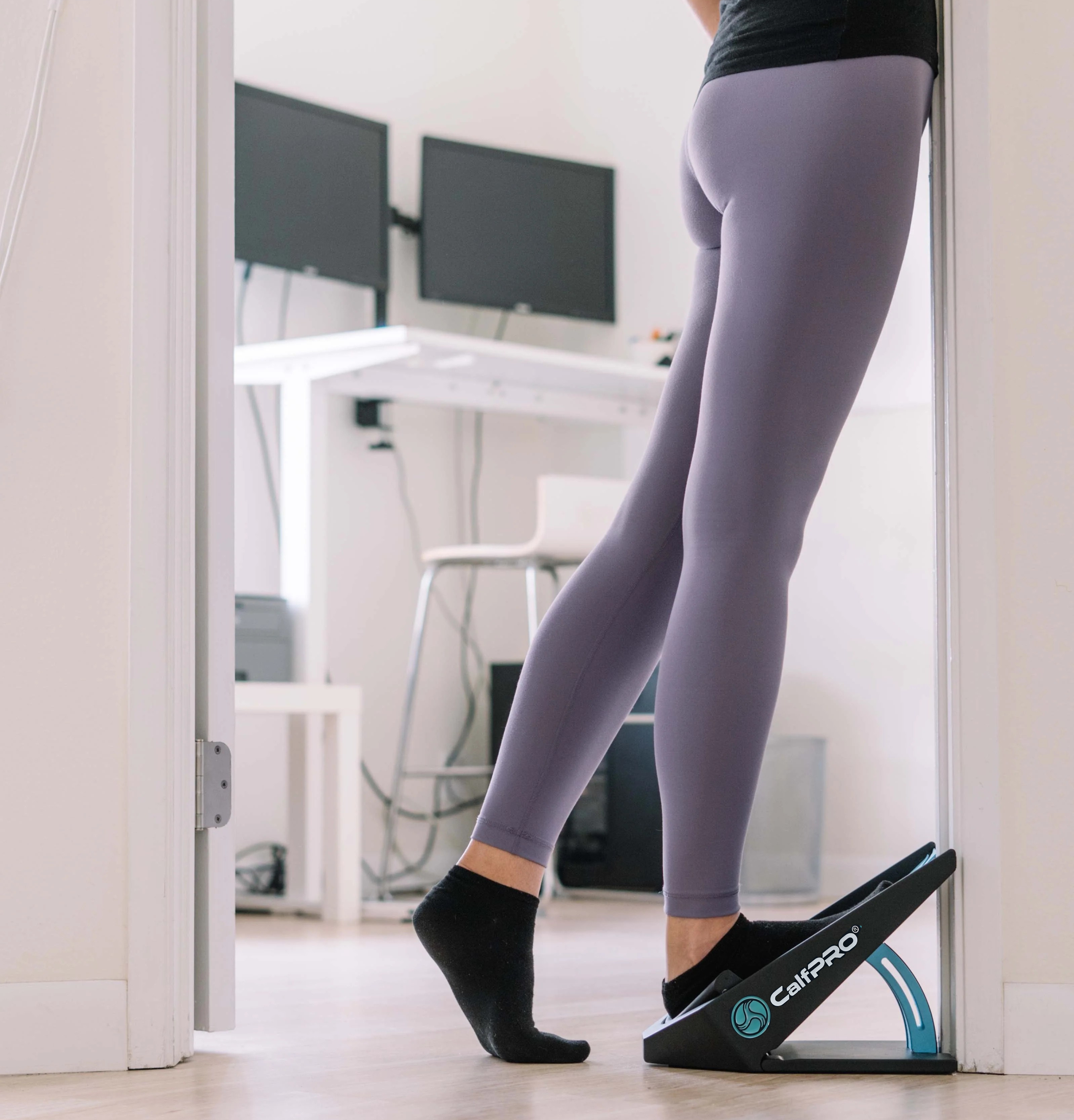 Person stretching calves using a slant board in a home office setting.