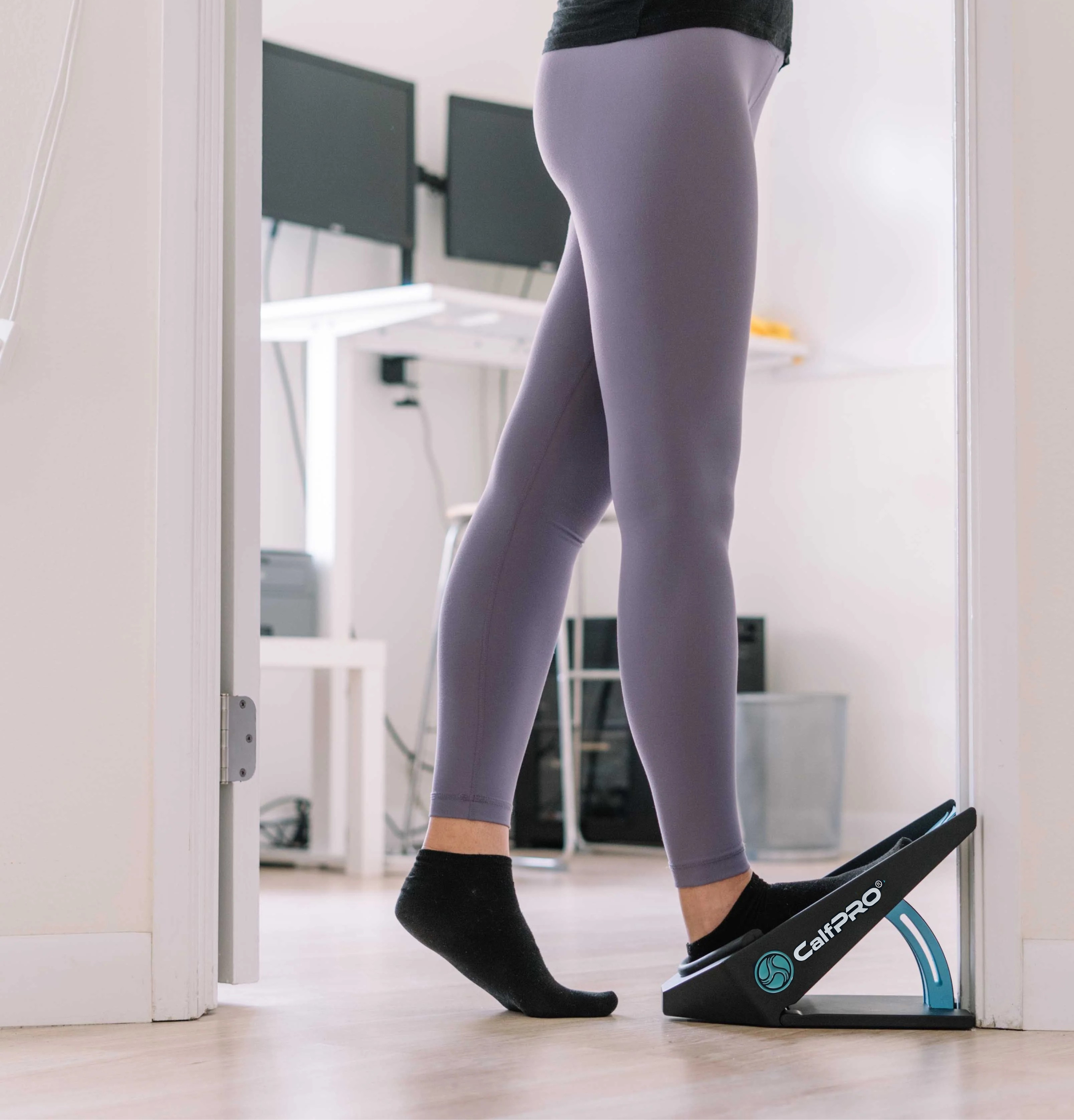 Person using a calf stretching board by a desk in an office setting.