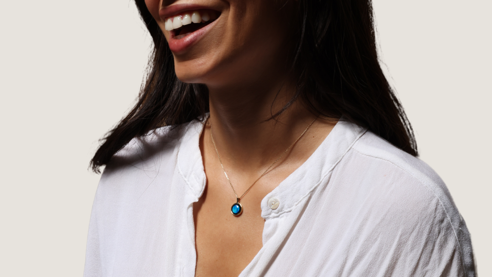 Woman wearing a white shirt and a blue pendant necklace, smiling.