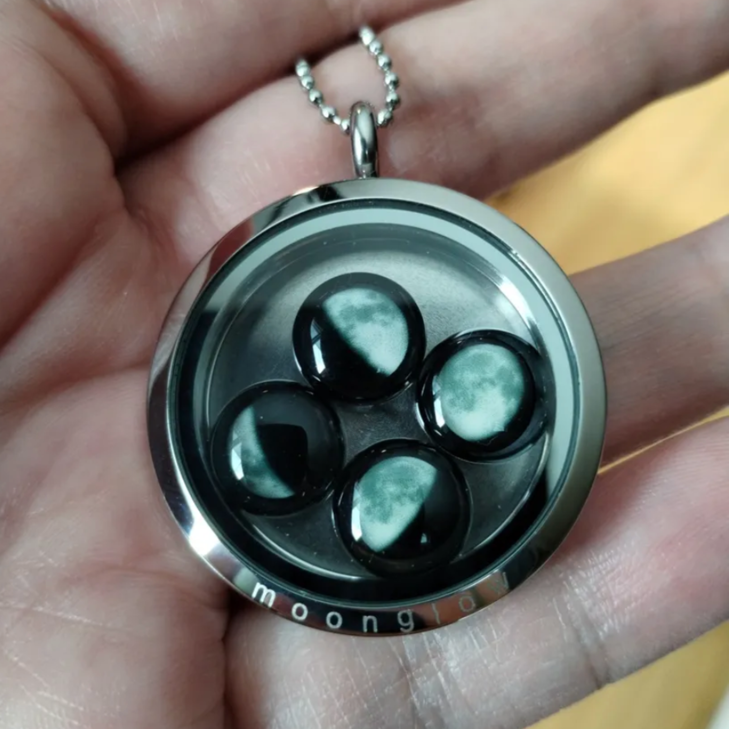 Hand holding a pendant with moon phase designs inside.