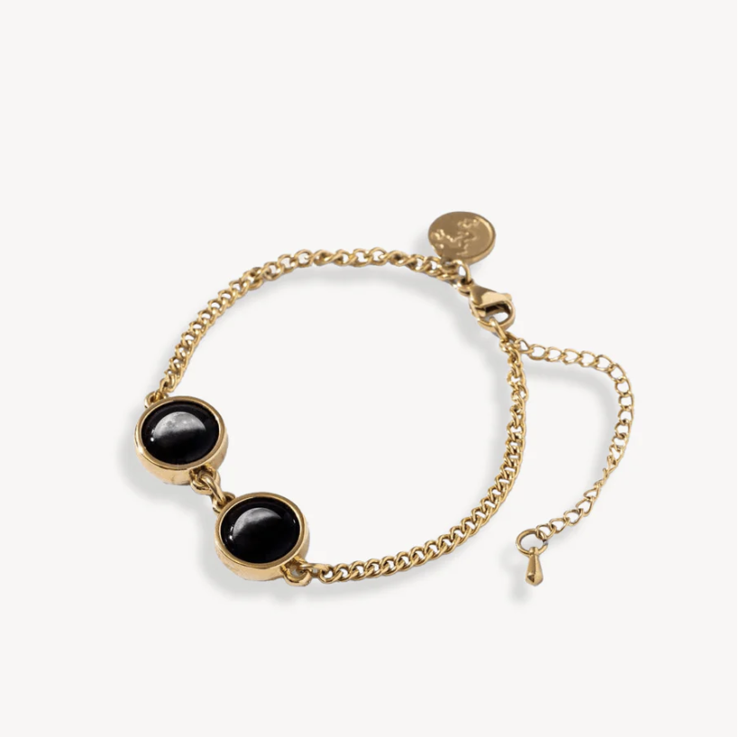 Gold chain bracelet with two black stones and a small round charm.