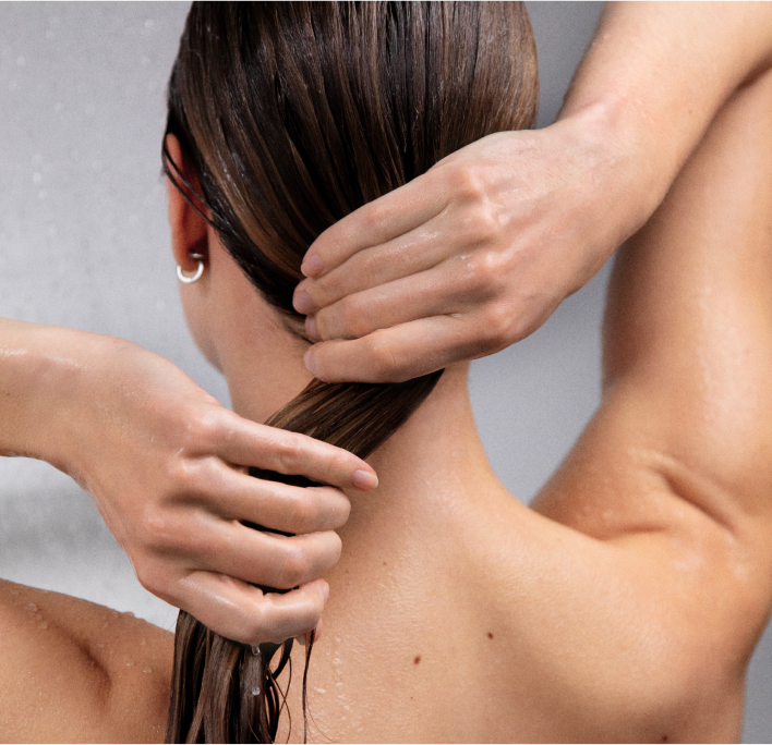 Person washing hair under shower, with hands gathering wet hair.